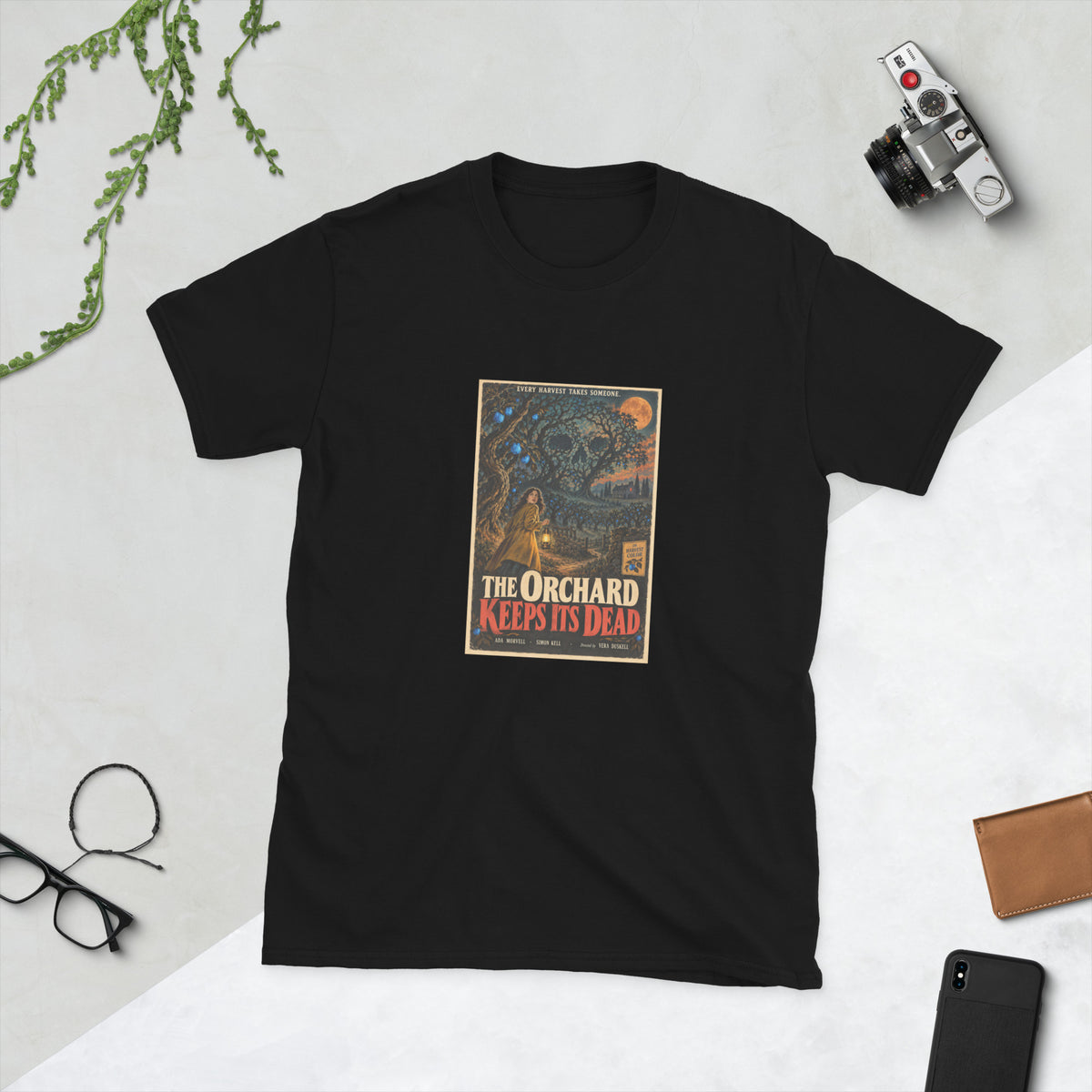 Black t-shirt printed with a vintage-style horror poster: a woman carrying a lamp through a twisted orchard whose branches form a giant skull under a copper moon, titled The Orchard Keeps Its Dead