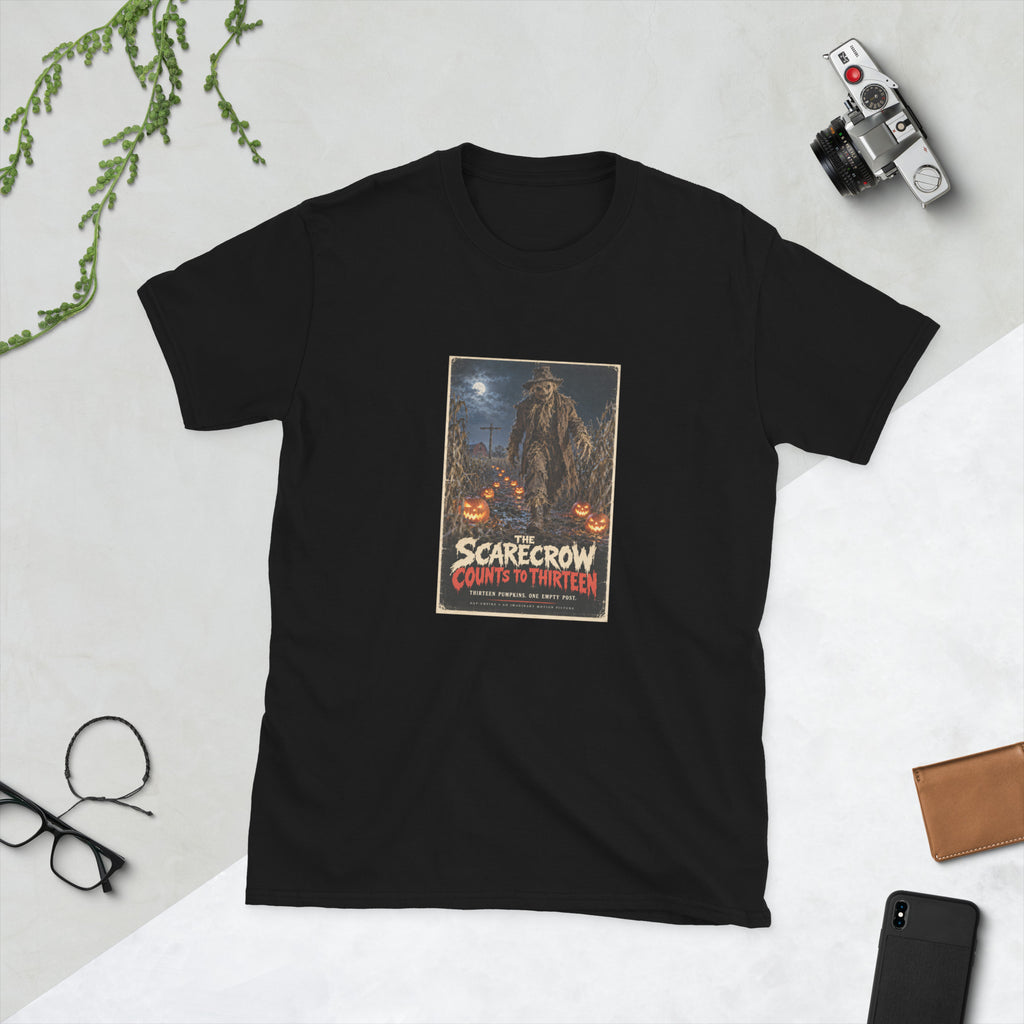 Black t-shirt printed with a horror movie poster of a tattered scarecrow walking down a muddy cornfield path lined with glowing jack-o'-lanterns, with a red barn and an empty wooden post under a full moon behind it, titled "The Scarecrow Counts to Thirteen."