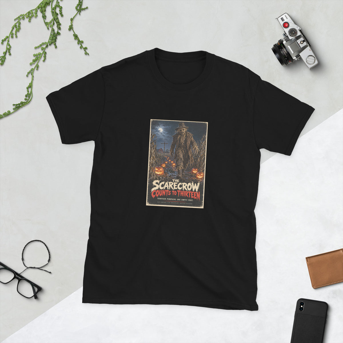 Black t-shirt printed with a horror movie poster of a tattered scarecrow walking down a muddy cornfield path lined with glowing jack-o'-lanterns, with a red barn and an empty wooden post under a full moon behind it, titled "The Scarecrow Counts to Thirteen."