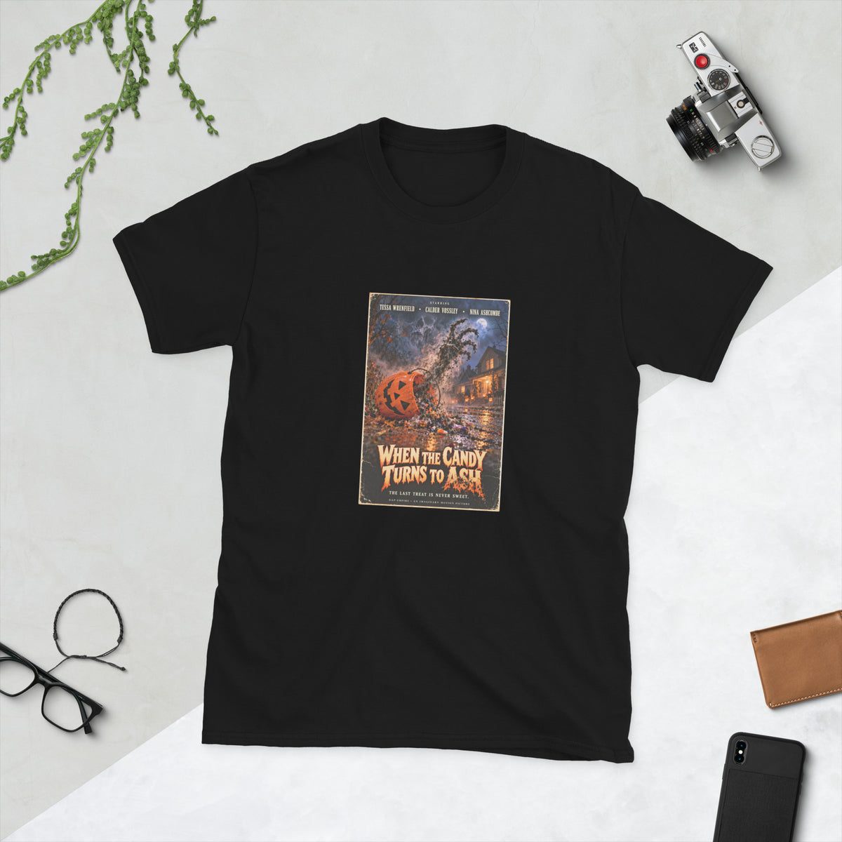 Black t-shirt printed with a horror movie poster of an orange jack-o'-lantern candy pail tipped over on a wet street, spilling wrapped candy as a skeletal hand of ash rises toward a full moon, under the orange title "When the Candy Turns to Ash."